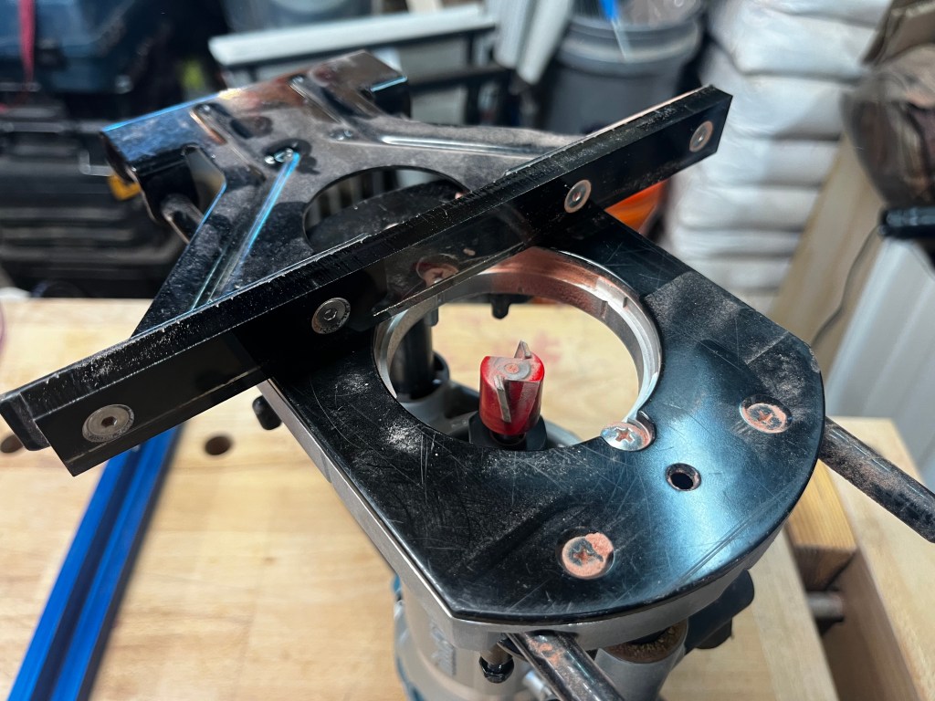 The underside of a palm router with fence attached. An acrylic piece is screwed onto the fence to eliminate the bit clearance gap in the fence.